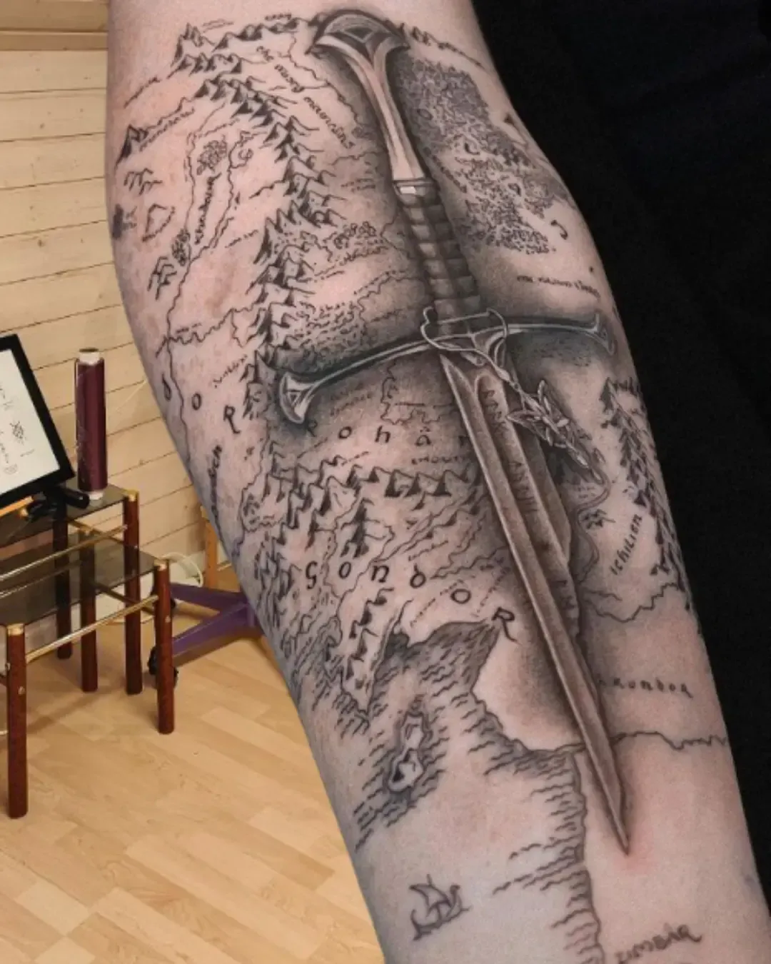 Tatouage épée du Seigneur des Anneaux posée sur la carte de la Terre du Milieu – design réaliste et épique, symbole de force et d’aventure, réalisé par Magic Ink à Fribourg.