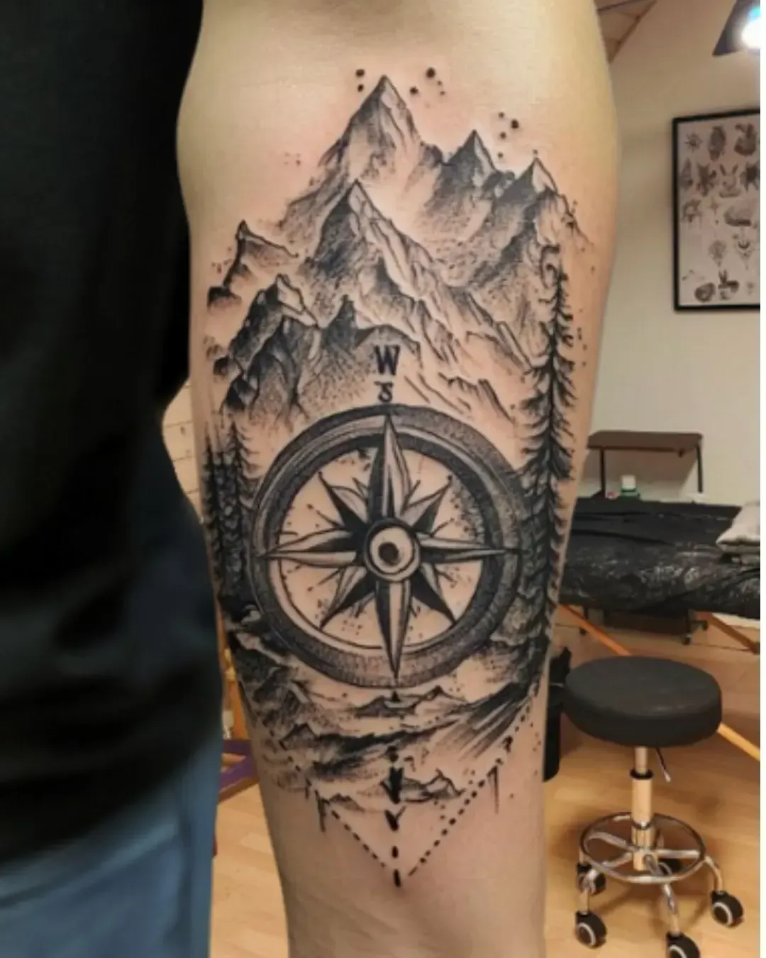 Tatouage réaliste de boussole et montagnes avec forêts – symbole de voyage, orientation et nature sauvage, réalisé par Magic Ink à Fribourg.
