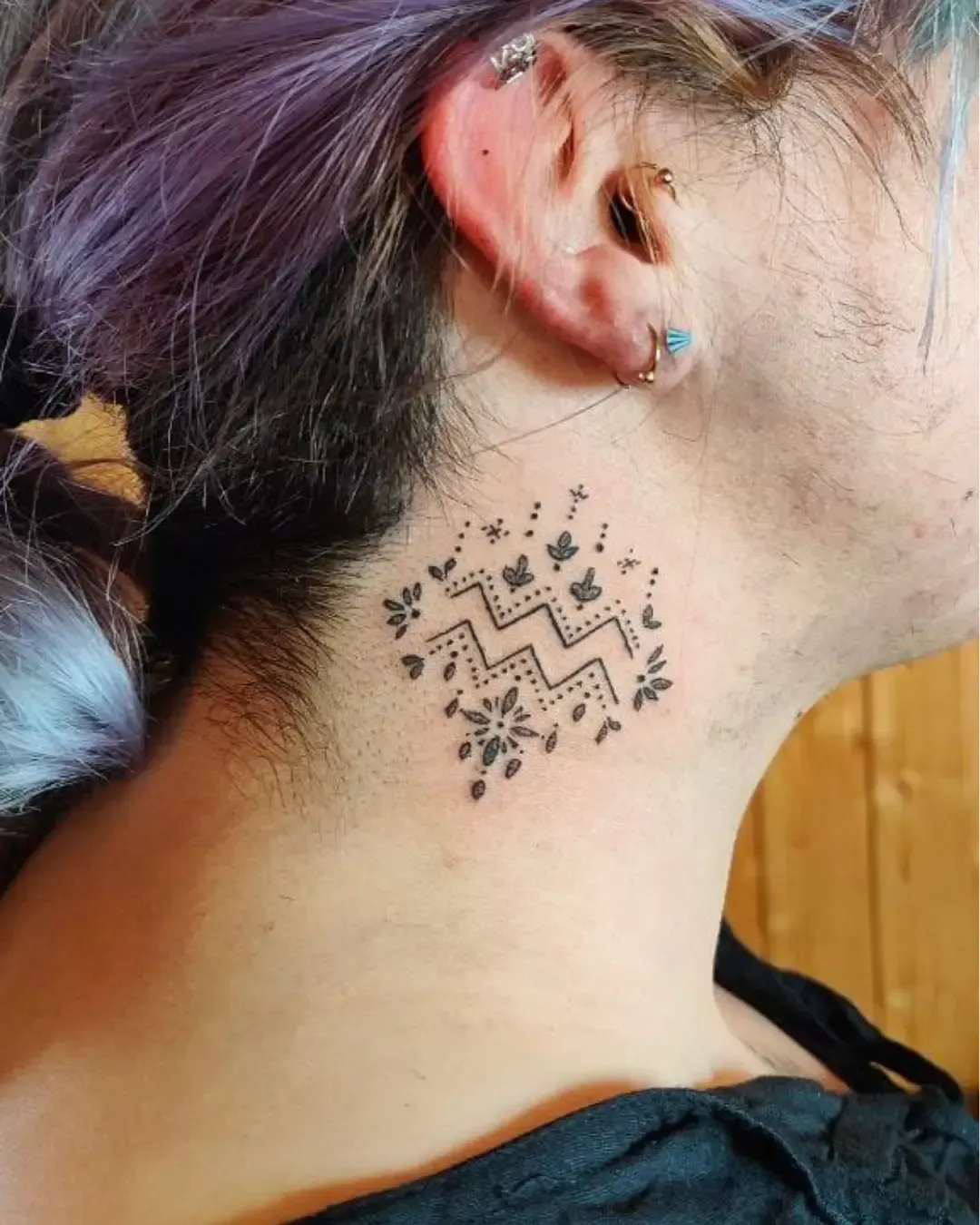 Tatouage minimaliste signe astrologique Verseau orné de fleurs et étoiles – symbole de créativité et liberté, réalisé par Magic Ink à Fribourg.