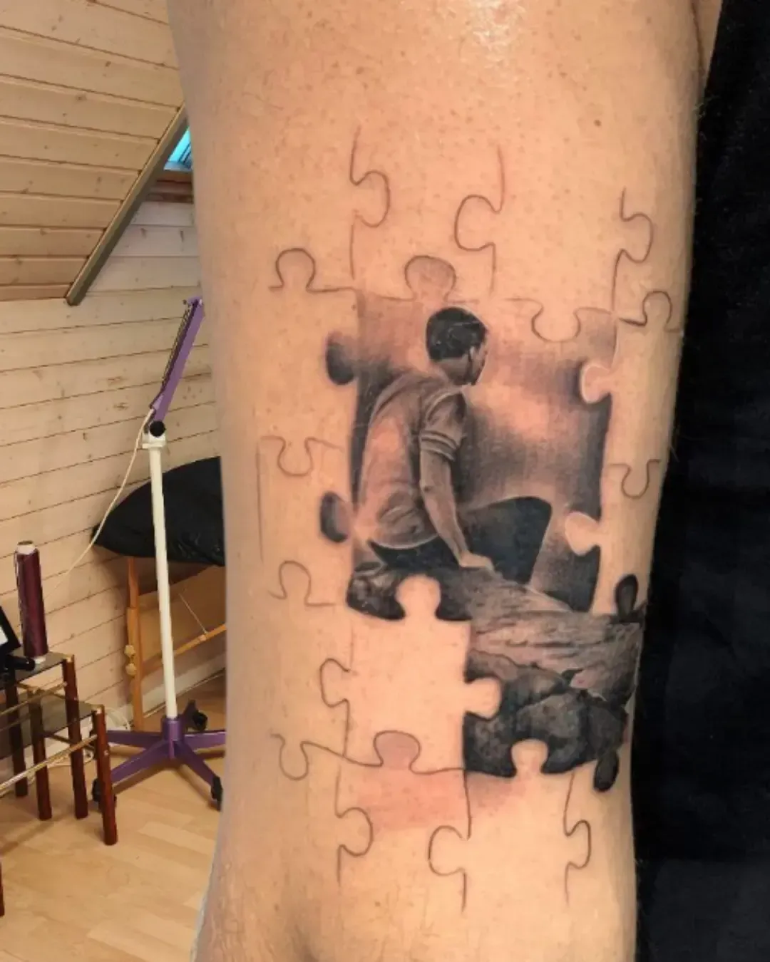 Tatouage réaliste en forme de puzzle représentant un homme assis – symbole de quête identitaire, pièces manquantes et introspection, réalisé par Magic Ink à Fribourg.