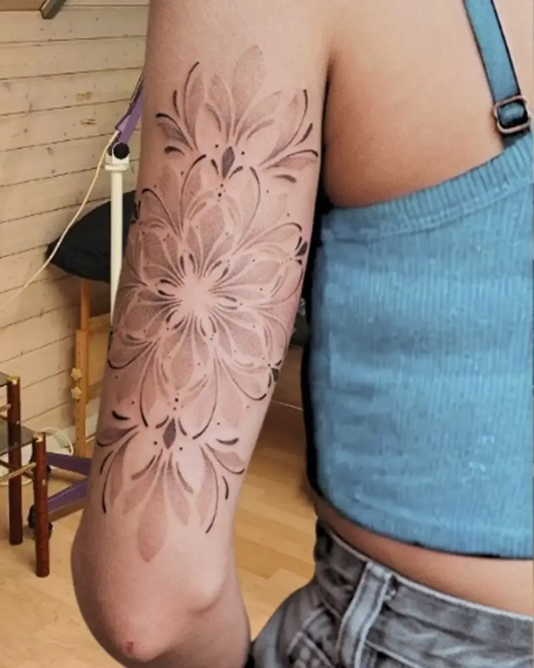 Tatouage ornemental floral réalisé sur le bras, avec un effet mandala délicatement travaillé en dégradé de points et de traits fins. Les pétales s’entrelacent pour former une composition géométrique et élégante qui épouse parfaitement la forme du bras. Une œuvre raffinée de Magic Tattoo Ink à Fribourg, idéale pour celles et ceux qui recherchent un design harmonieux, féminin et intemporel.
