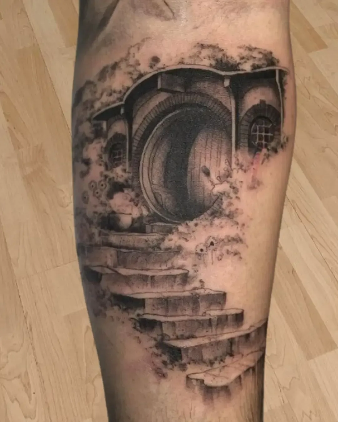 Tatouage réaliste d’une maison de Hobbit inspirée du Seigneur des Anneaux – porte ronde, escaliers et ambiance féérique, réalisé par Magic Ink à Fribourg.