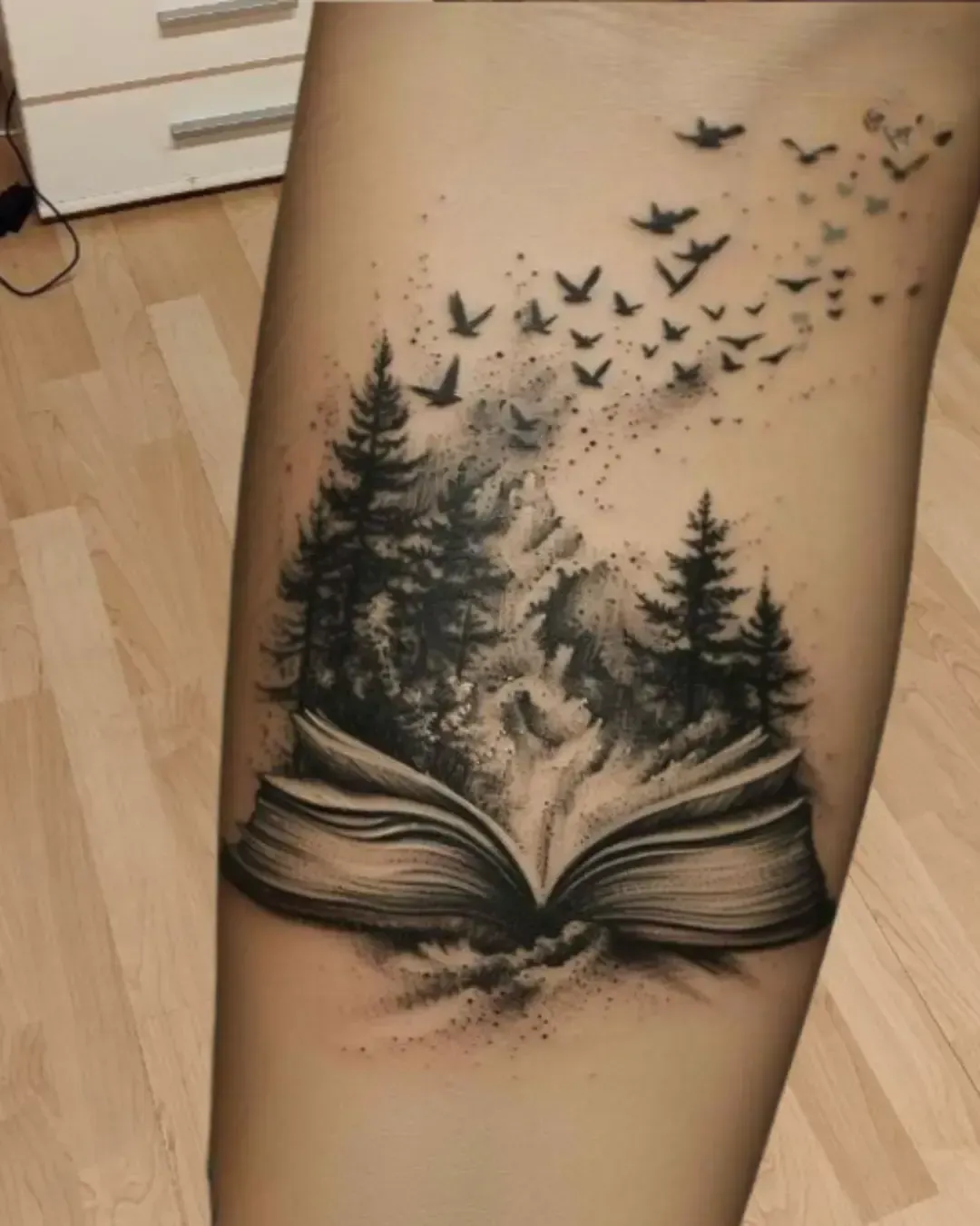 Tatouage artistique d’un livre ouvert laissant s’échapper une forêt et des oiseaux – symbole d’imaginaire, liberté et évasion, réalisé par Magic Ink à Fribourg.
