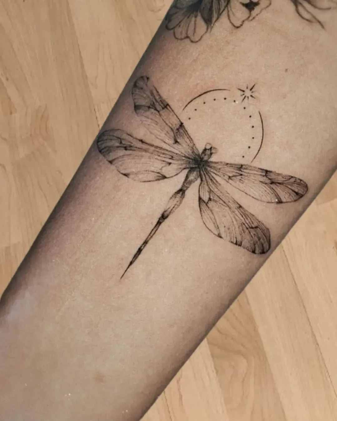 Tatouage libellule fine en noir et gris avec croissant de lune et étoile – symbole de légèreté, transformation et liberté, photo réalisée sur tatouage cicatrisé par Magic Ink à Fribourg.