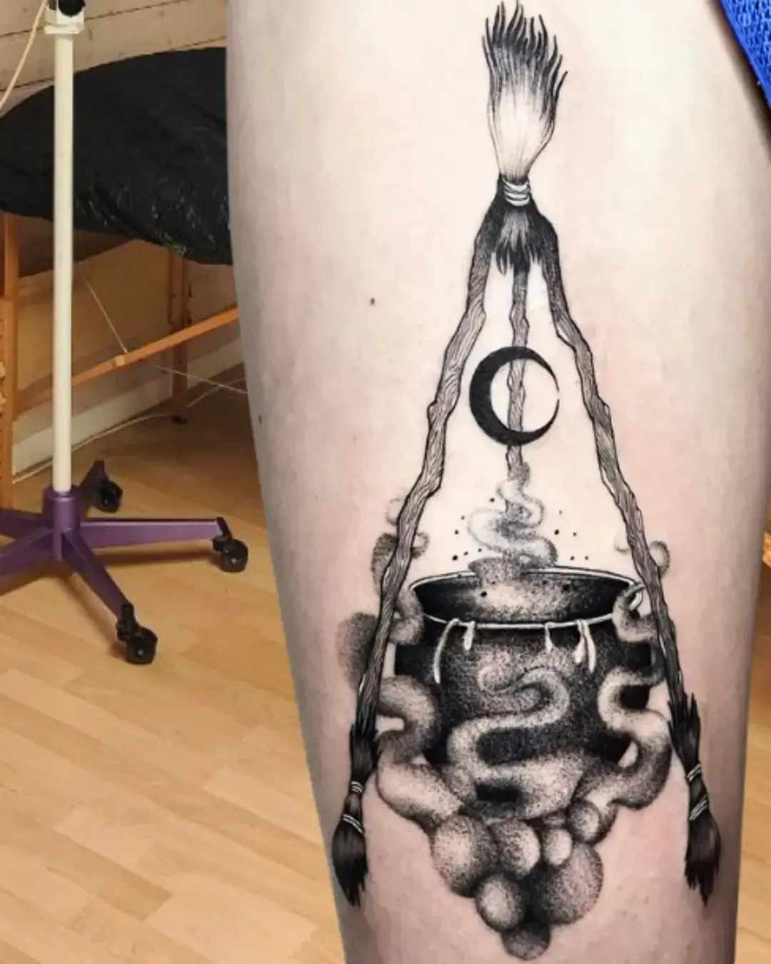 Tatouage chaudron de sorcière fumant avec croissant de lune et deux tresses formant un triangle – symbole de magie, alchimie et mysticisme, réalisé par Magic Ink à Fribourg.
