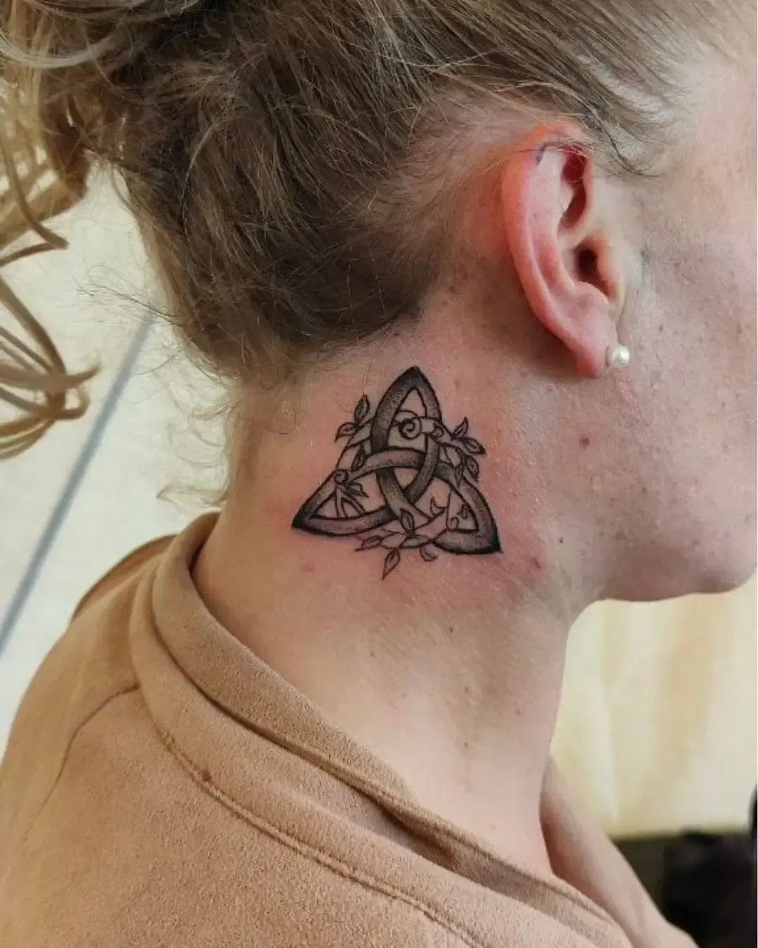 Tatouage triquetra celtique orné de branches et feuilles – symbole d’éternité, spiritualité et connexion à la nature, réalisé par Magic Ink à Fribourg.