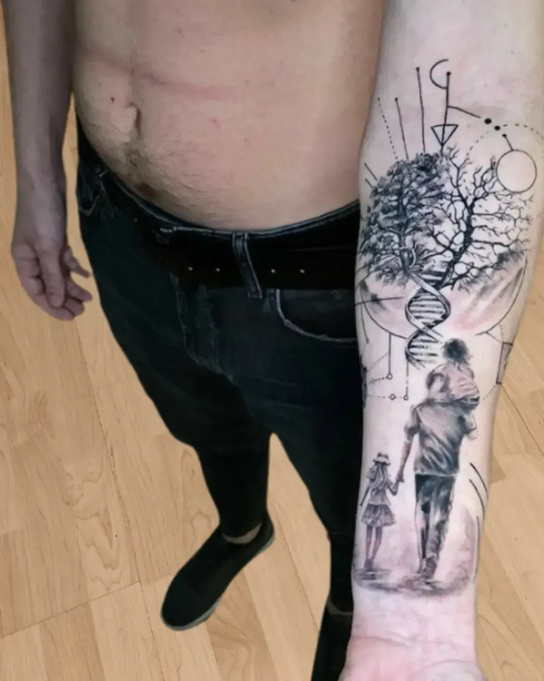 Tatouage réaliste sur l’avant-bras représentant un père avec deux enfants, accompagné d’un arbre de vie relié à une spirale d’ADN et entouré de motifs géométriques.