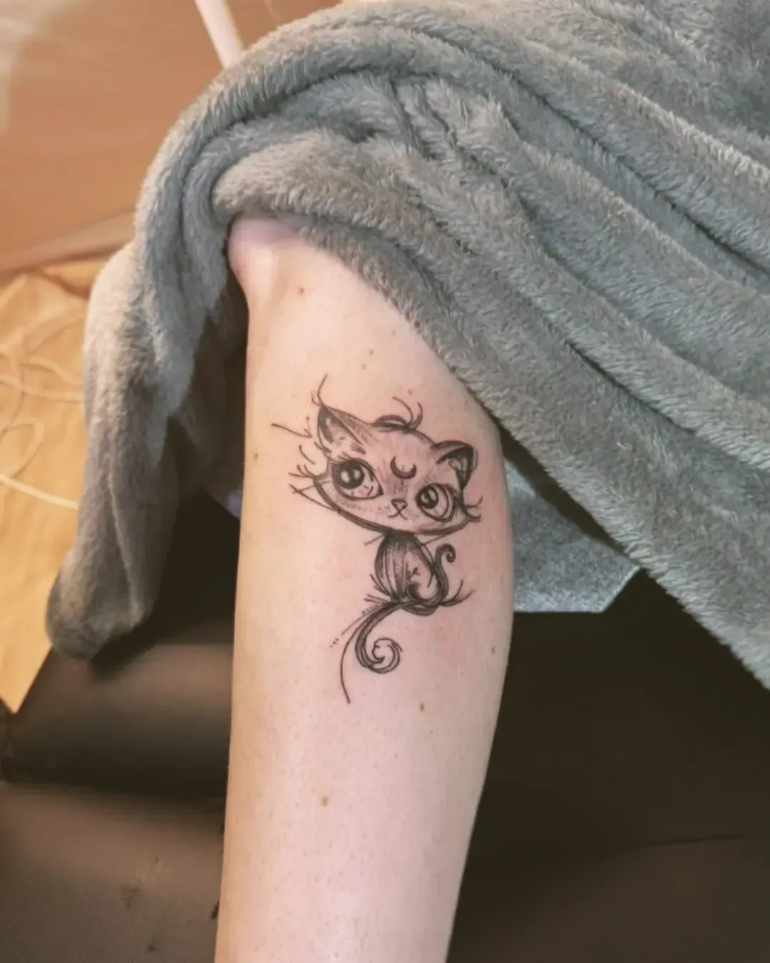 Tatouage de petit chat stylisé aux grands yeux avec croissant de lune – design mignon et magique, réalisé par Magic Ink à Fribourg.