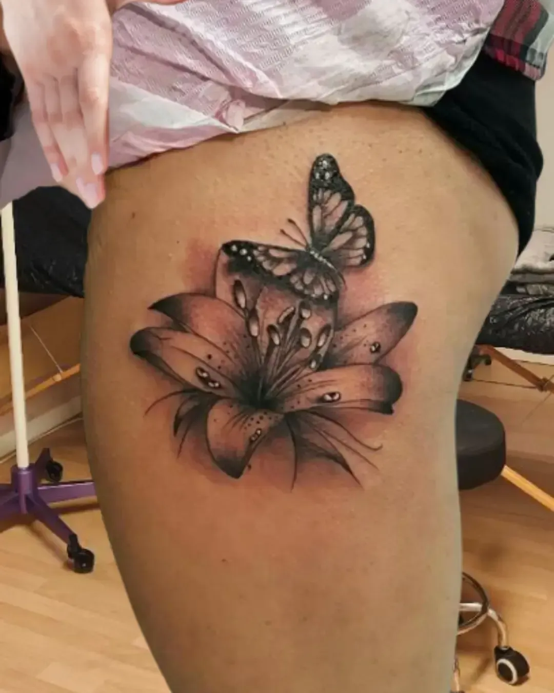 Tatouage réaliste de papillon posé sur une fleur avec gouttes de rosée – symbole de beauté, transformation et renaissance, réalisé par Magic Ink à Fribourg.