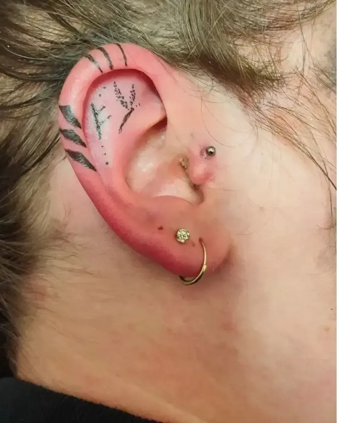 Tatouage discret dans l’oreille mêlant motifs végétaux et traits géométriques fins, créant un effet ornemental élégant et original.