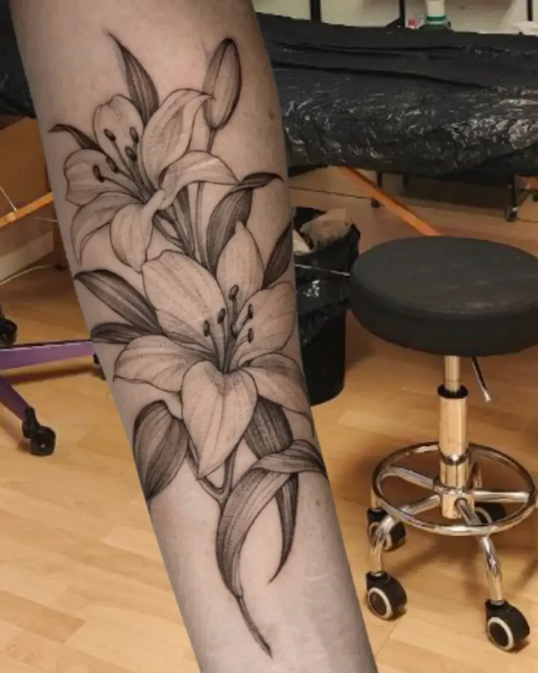 Tatouage floral de lys en noir et gris – symbole de pureté, élégance et renaissance, réalisé par Magic Ink à Fribourg en Suisse.