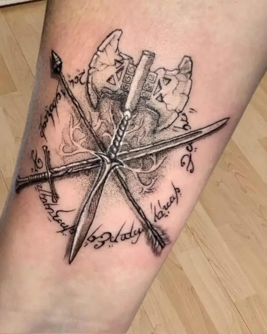 Tatouage artistique avec hache viking et épées croisées, entourées de runes nordiques et d’écriture elfique – symbole de puissance et héritage mystique, réalisé par Magic Ink à Fribourg.