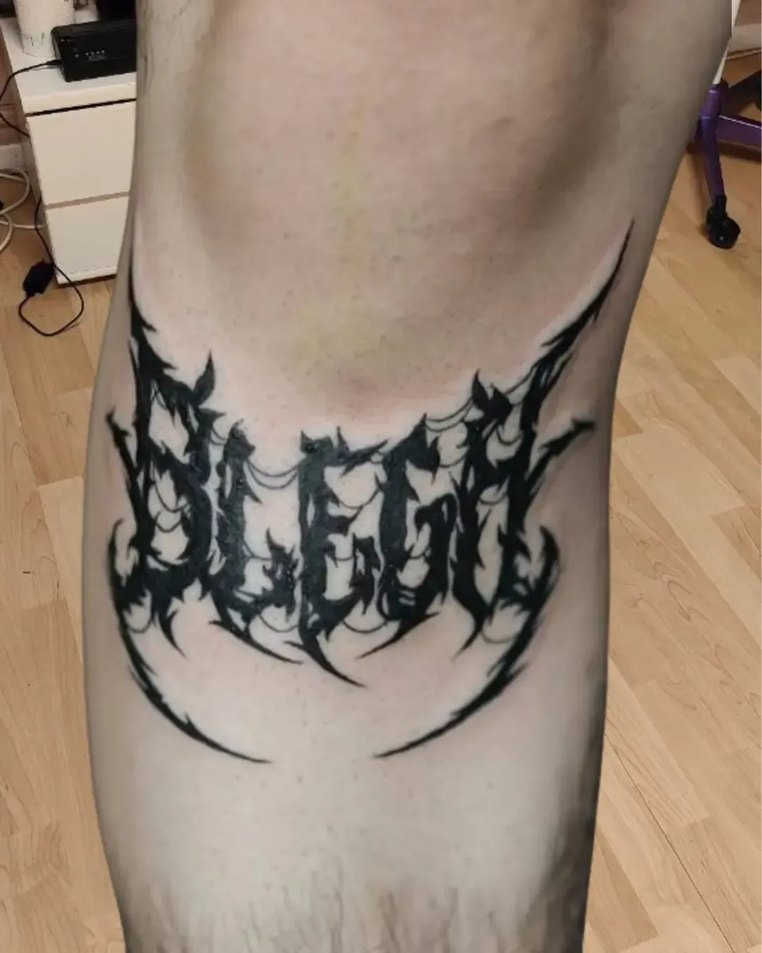 Tatouage lettering en style blackwork agressif et anguleux, formant le mot "Slegh", inspiré de l’esthétique métal extrême et des logos de groupes de heavy/black metal.