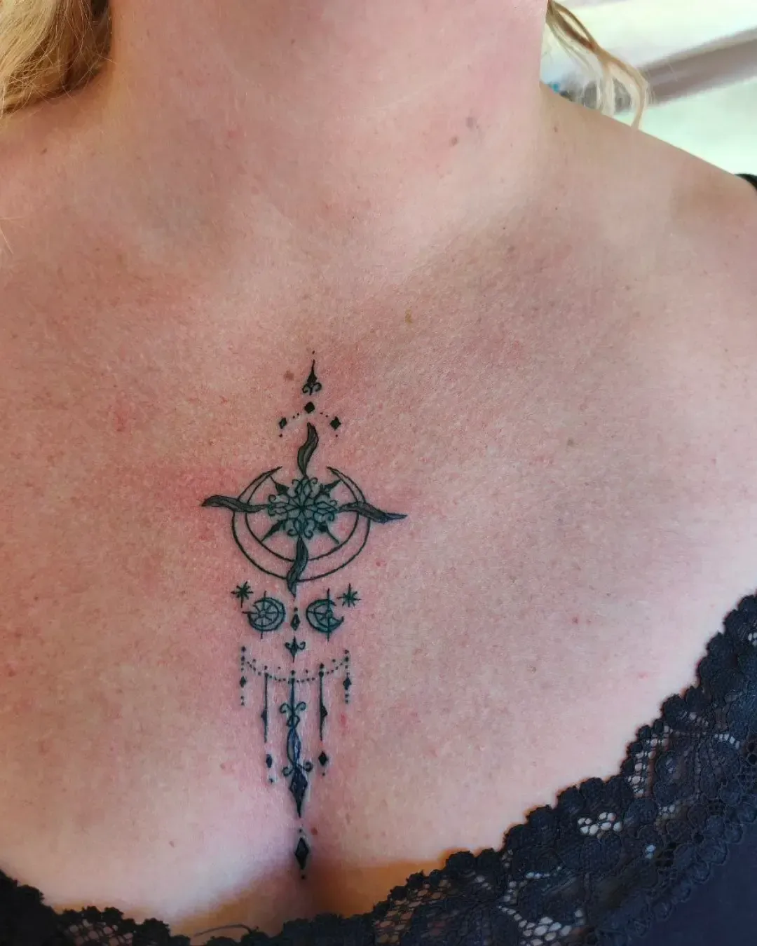Tatouage ornemental délicat au centre du décolleté – mélange de motifs géométriques, lunes et perles suspendues, créant une composition élégante et féminine, réalisé par Magic Ink à Fribourg.