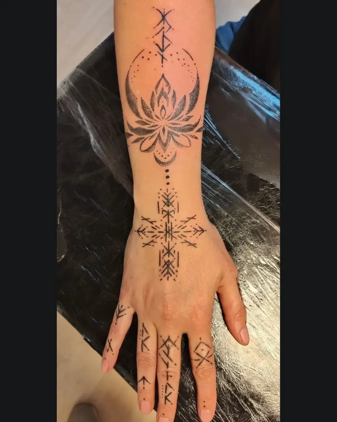 Tatouage ornemental main et avant-bras en dotwork avec motifs runiques et fleur de lotus – symbolique spirituelle et nordique, réalisé par Magic Ink à Fribourg en collaboration avec Griffes du Nord.
