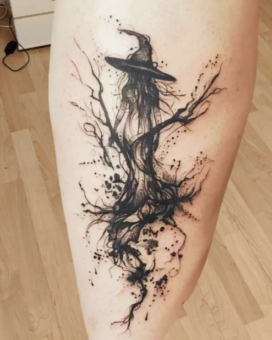 Tatouage artistique de sorcière au chapeau pointu en style aquarelle et traits abstraits – symbole de mystère, magie et féminité, réalisé par Magic Ink à Fribourg.