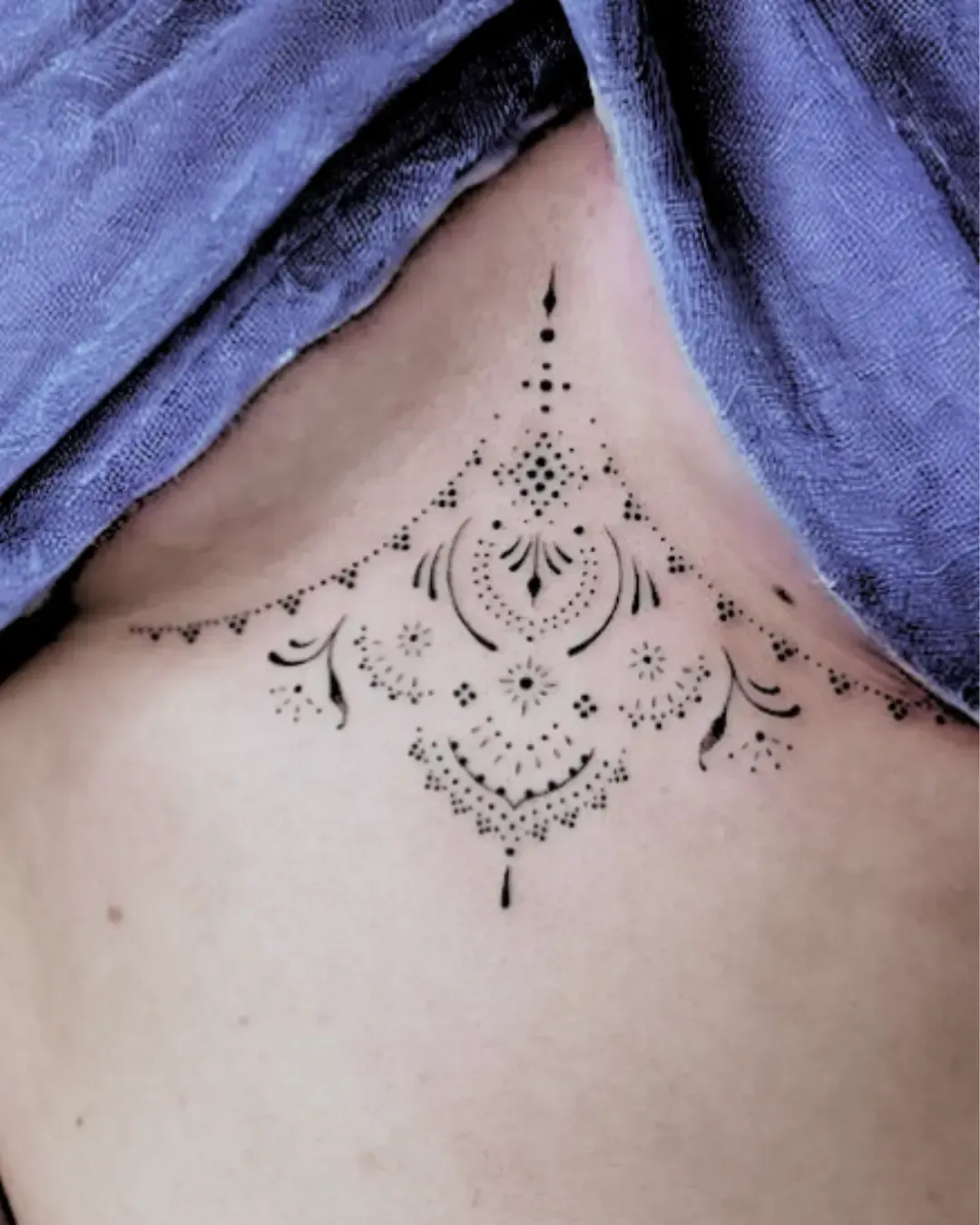 Tatouage ornemental finement réalisé sous la poitrine – composé de motifs géométriques, pointillés et arabesques délicates, créant un effet de dentelle raffinée. Un design élégant et sensuel signé Magic Ink à Fribourg.