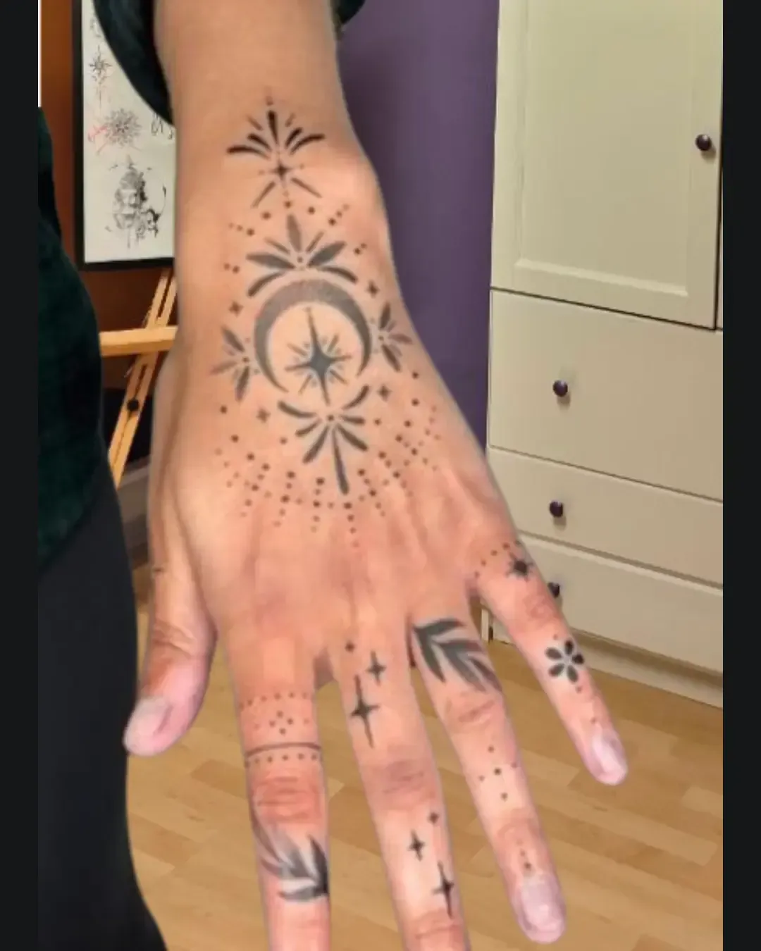 Tatouage mystique et ornemental sur la main, combinant une lune en croissant, une étoile centrale rayonnante et des motifs géométriques en pointillés ✨🌙. Les doigts sont décorés de symboles fins – petites étoiles, feuilles et fleurs – donnant un rendu à la fois élégant, spirituel et raffiné. Un design parfait pour celles et ceux qui souhaitent porter un talisman protecteur et esthétique au quotidien. Réalisé par Magic Tattoo Ink à Fribourg.
