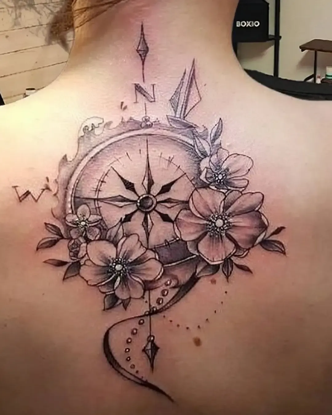 Tatouage boussole ornementale avec fleurs et perles, placé entre les omoplates – un design symbolisant le voyage, la direction et l’harmonie, réalisé par Magic Ink à Fribourg.