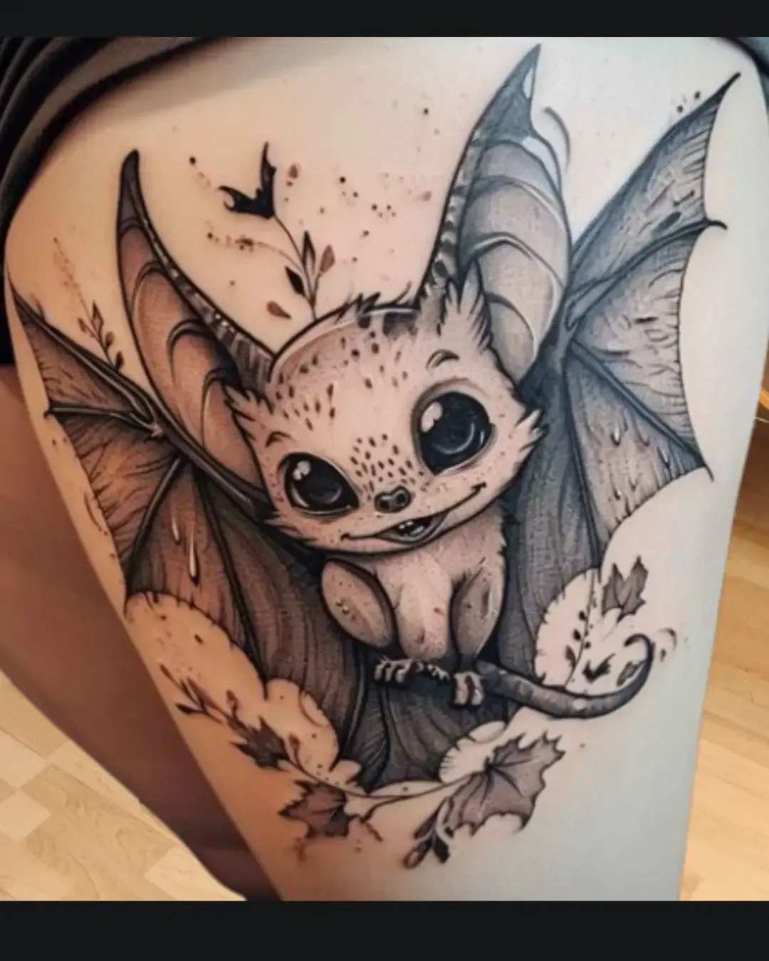 Tatouage d’une petite chauve-souris au style kawaii, avec de grands yeux expressifs et un sourire malicieux. Perchée sur une branche entourée de feuilles, elle déploie ses ailes finement détaillées dans un jeu d’ombres et de lumière. Ce design original mélange réalisme et douceur, idéal pour celles et ceux qui souhaitent un tatouage à la fois mignon et mystérieux, signé Magic Tattoo Ink à Fribourg.