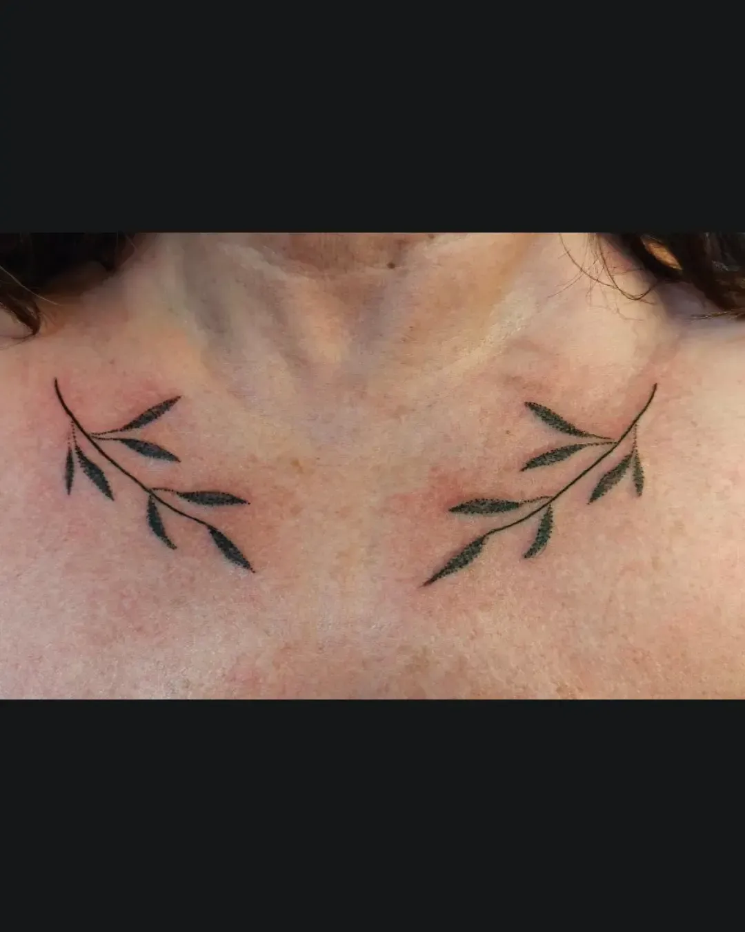 Tatouage dotwork minimaliste de branches d’olivier en noir, symétriques sur le haut de la poitrine – création fine et élégante par Magic Tattoo Ink à Fribourg, Suisse