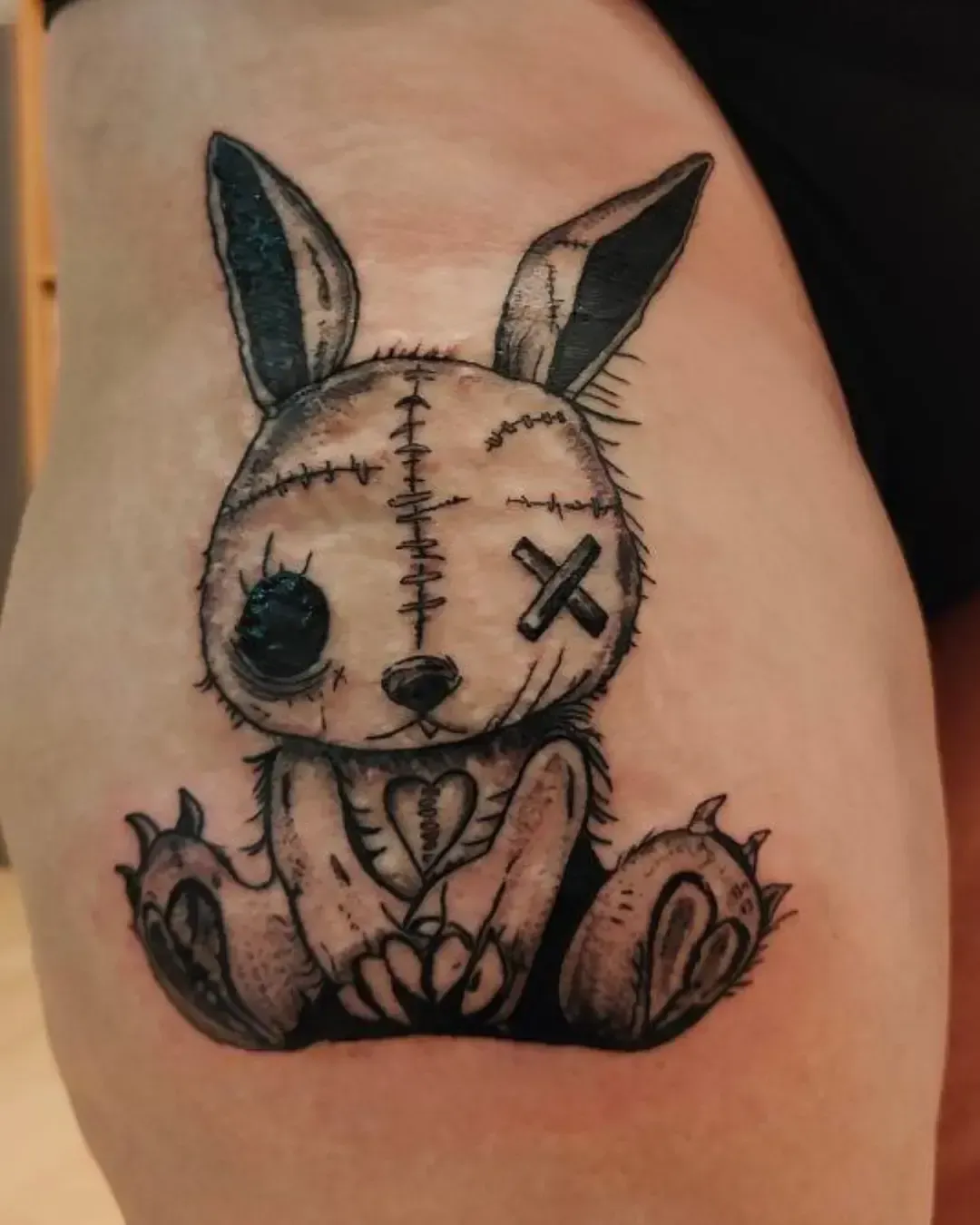 Tatouage lapin en peluche style gothique et cousu, noir et gris, avec cicatrices et cœur brodé – création artistique Magic Tattoo Ink à Fribourg, Suisse