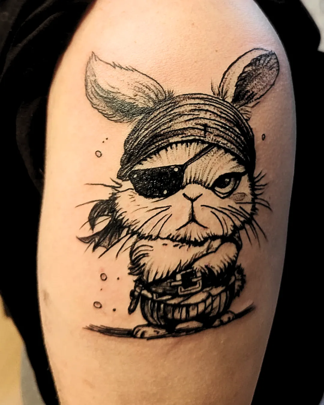 Tatouage humoristique et original représentant un lapin pirate. Avec son bandana, son cache-œil et sa ceinture de flibustier, ce petit personnage allie mignonnerie et côté rebelle. Le style en noir et gris, avec un trait vif et des ombrages subtils, donne du caractère et de la personnalité à ce dessin unique.