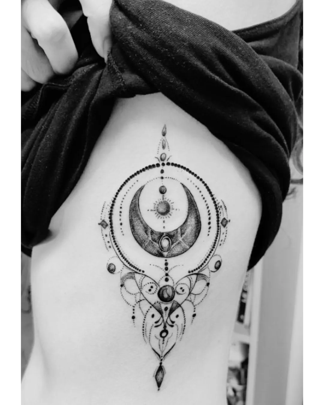 Tatouage ornemental et spirituel représentant une lune croissante entourée d’éléments cosmiques. Le design mêle géométrie sacrée, mandala et dotwork, créant un équilibre parfait entre finesse et puissance. Les détails de perles et d’arabesques accentuent la fluidité et la féminité du motif, tandis que la lune centrale incarne la renaissance, l’intuition et le cycle de la vie.