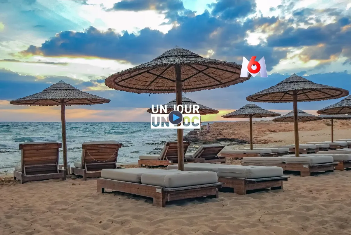 Plage premium au coucher du soleil avec transats en bois, parasols exotiques et vue mer, visuel du reportage Un Jour Un Doc sur M6 consacré aux vacances et clubs de voyage