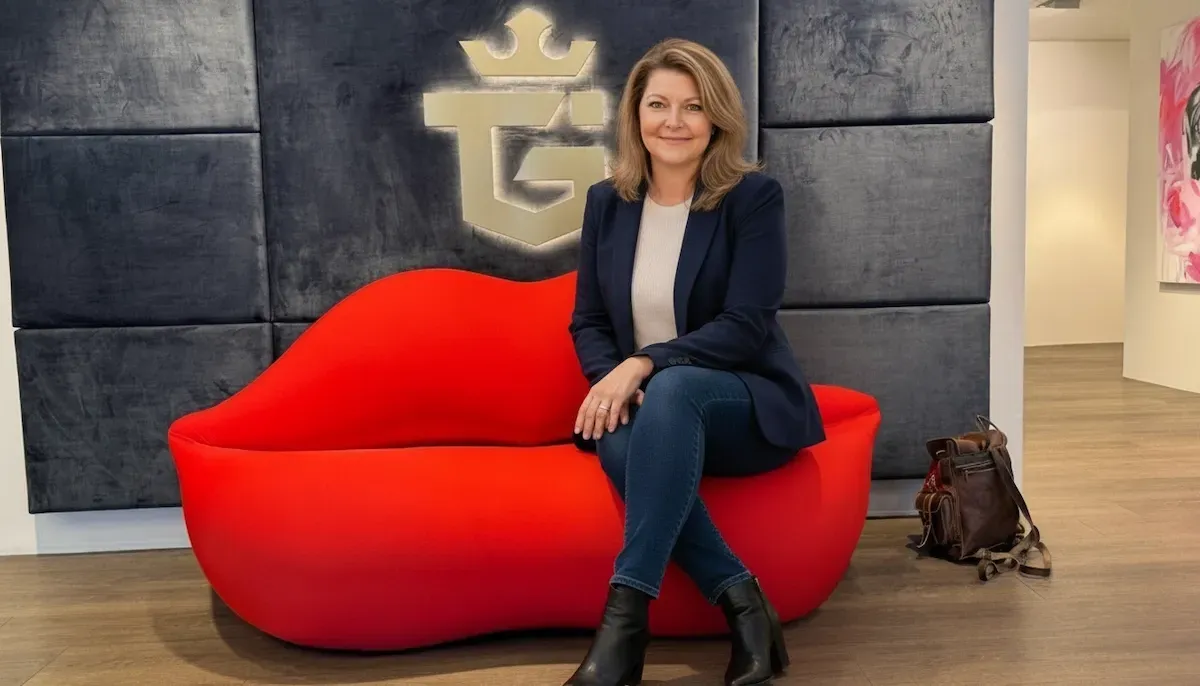 Annemarie Andrey assise dans les locaux TGI devant le logo de la société spécialisée dans l’investissement en or physique et la protection du capital