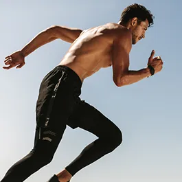 Fit man sprinting in athletic gear against a clear sky, showing strength, determination, and peak performance.