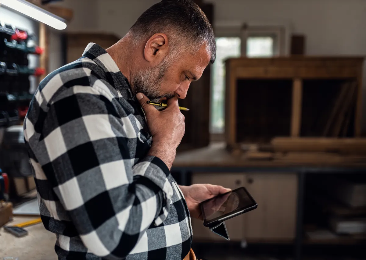 Business owner checking his phone in a cluttered home service workshop
