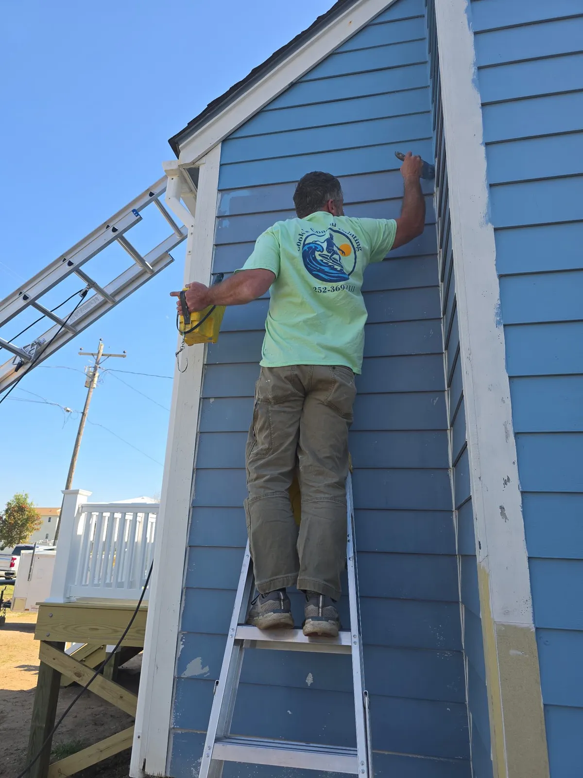 Painter applying fresh paint to blue lap siding on a Morehead City home