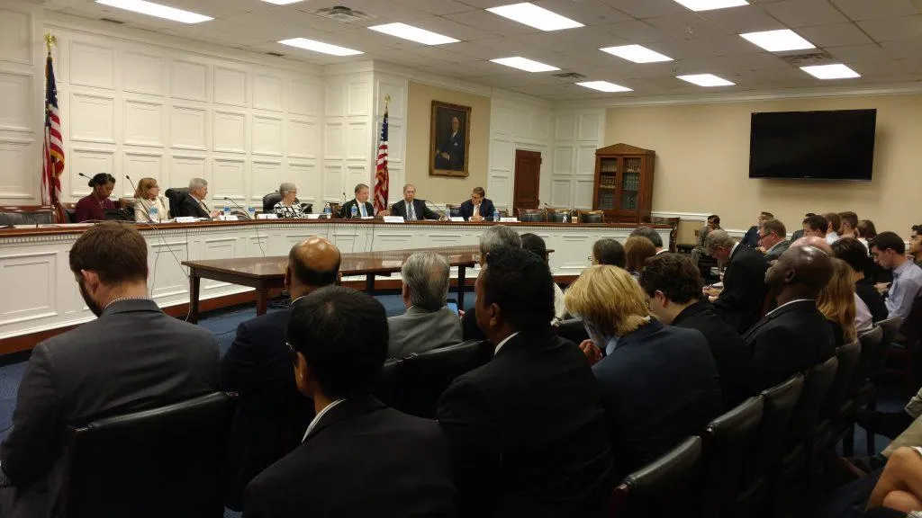 A group of individuals seated at a table in a room, appearing to be in a meeting or conference setting