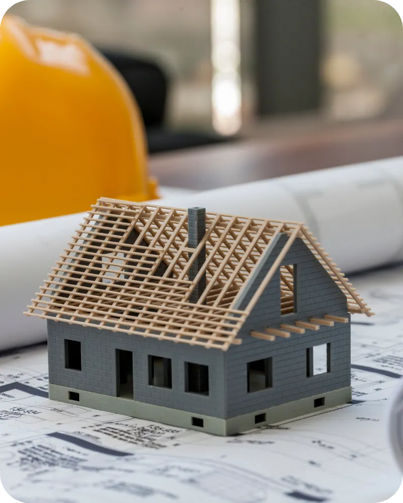 Miniature model of a partially constructed house next to blueprints and a hard hat, illustrating the importance of new construction phase inspections in Nashville and Middle Tennessee.