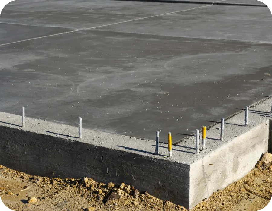 Concrete foundation slab with visible footing and anchor points at a residential construction site, illustrating components evaluated during a Phase 1 Foundation Inspection.