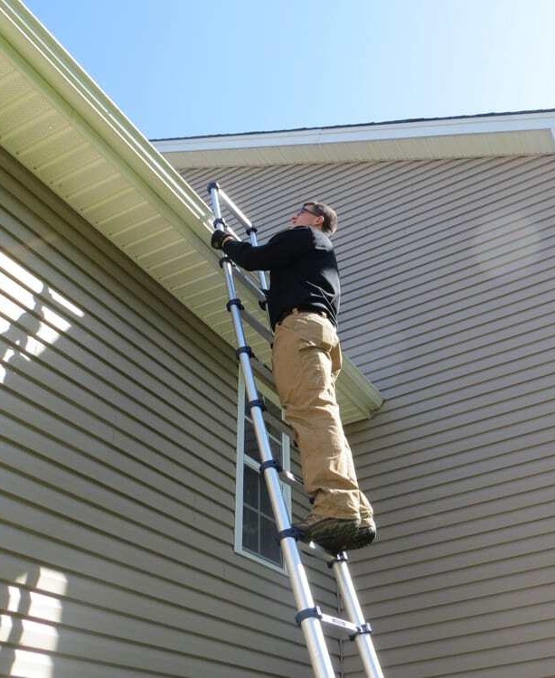 Professional home inspector using a ladder to inspect exterior siding and roof eaves of a residential home