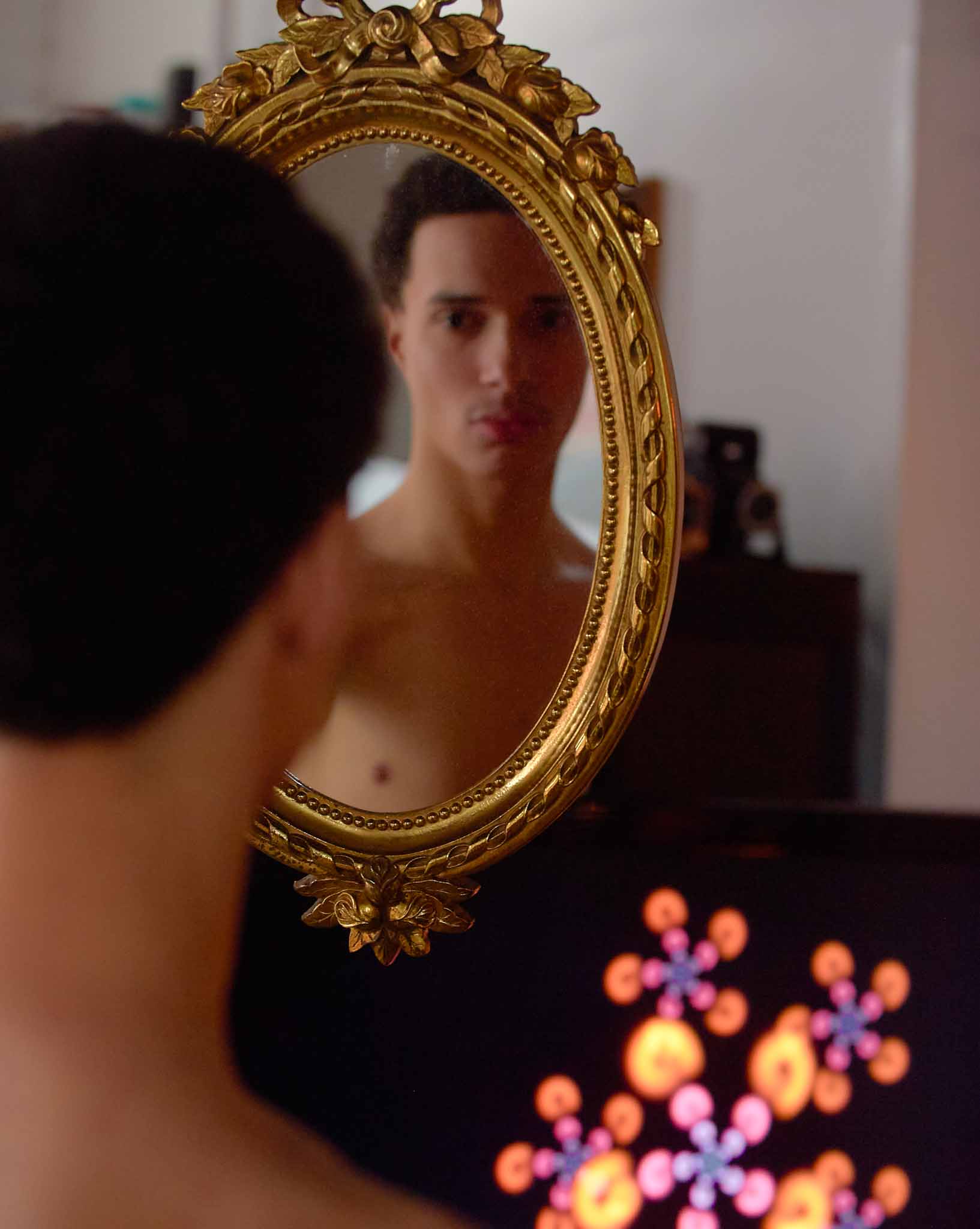 Young man looking into a hand mirror, slightly brighter lighting.