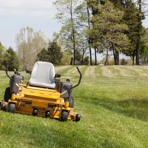 A yellow lawn mower about to cut grass in a giant field