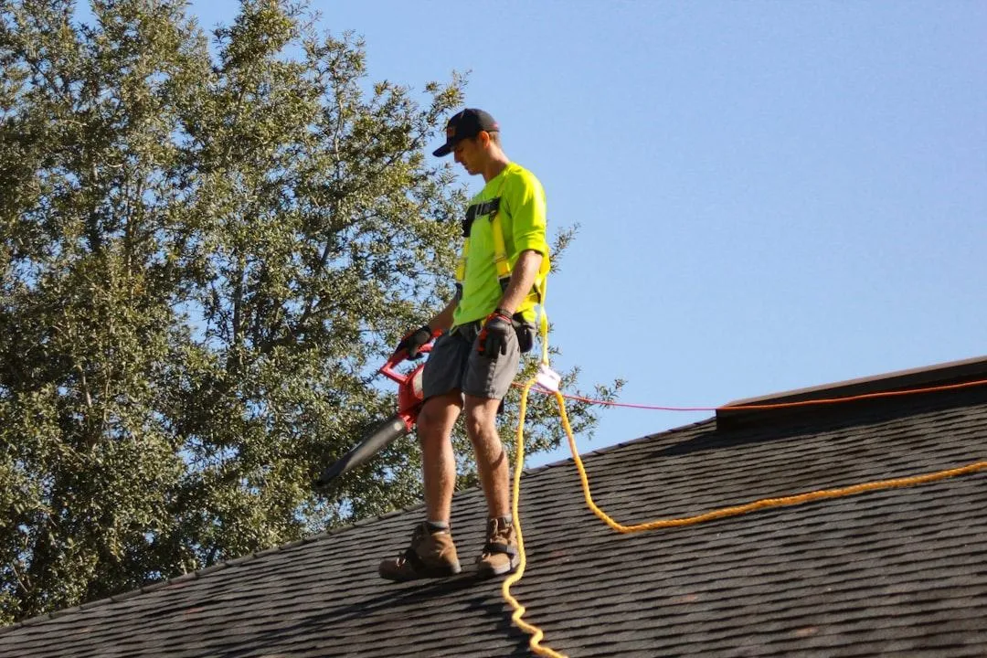 Roofer standing on a house roof with safety gear and tools, preparing for repair work, symbolizing roofing contractors and storm damage services.