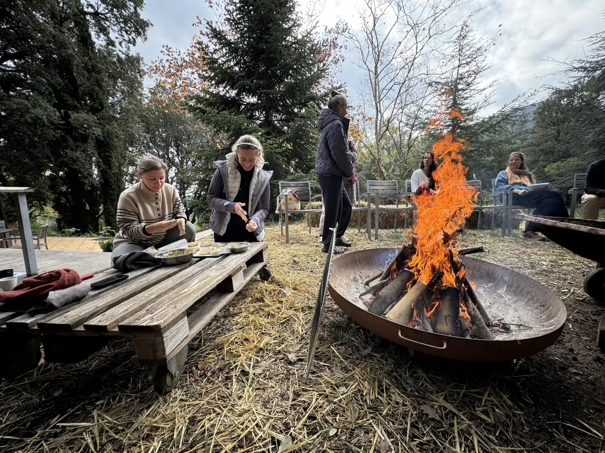 Sabrina Stocker sitting with a sister by a glowing fire in the woodlands, sharing warmth and connection during a cacao ceremony.