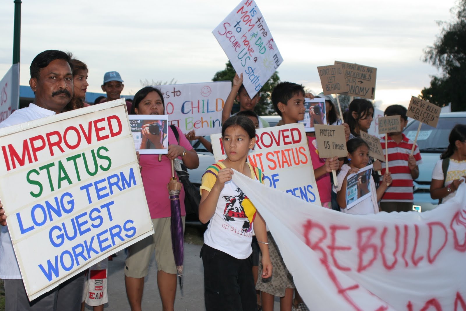 Foreign workers and their children hold up signs and banners to advocate for improved status in the CNMI.