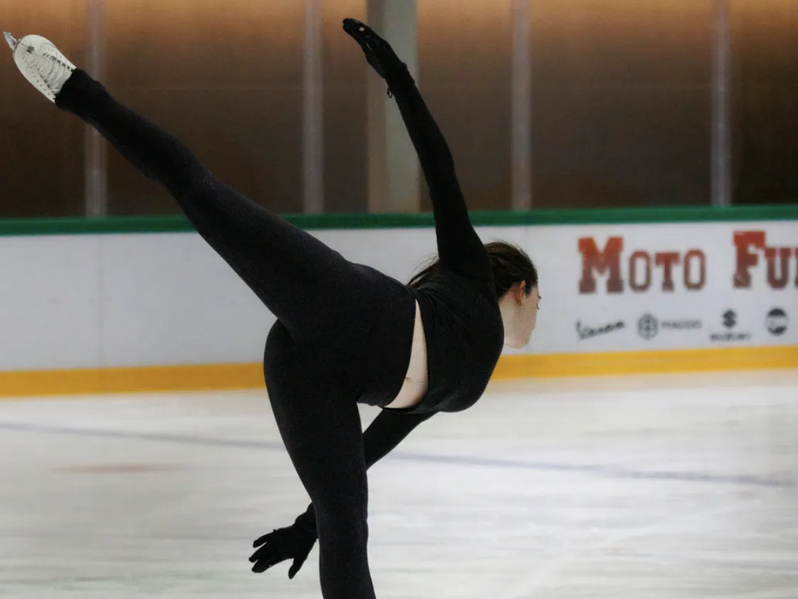 Young figure skater in tan and blue outfit performing a spiral on ice