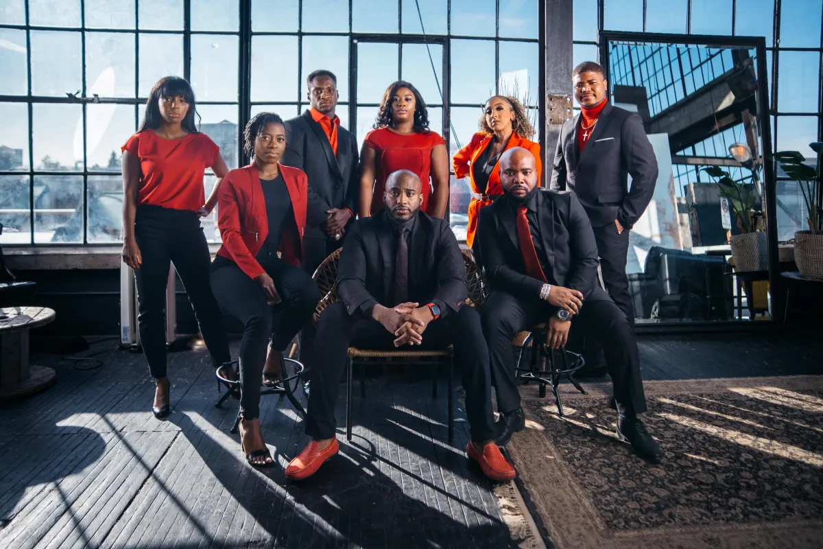 A professional Black Canadian real estate broker stands confidently with a diverse brokerage team in a modern office lobby. Everyone is dressed in business attire, smiling, and exuding trust and expertise. The background features subtle Ontario real estate imagery, 3:2 aspect ratio.