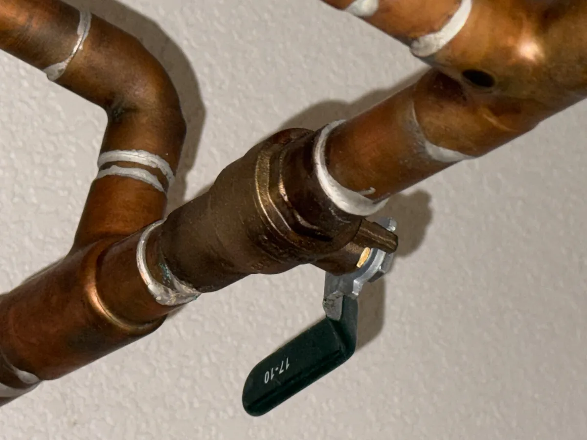 Illustrative photograph of copper water pipes and a shutoff valve with a green handle. Your home's arrangement may differ.