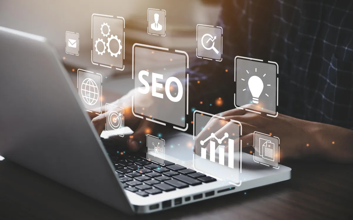 Close-up of hands typing on a laptop with floating digital icons representing SEO, analytics, content, and web tools, symbolizing search engine optimization and digital marketing strategies.