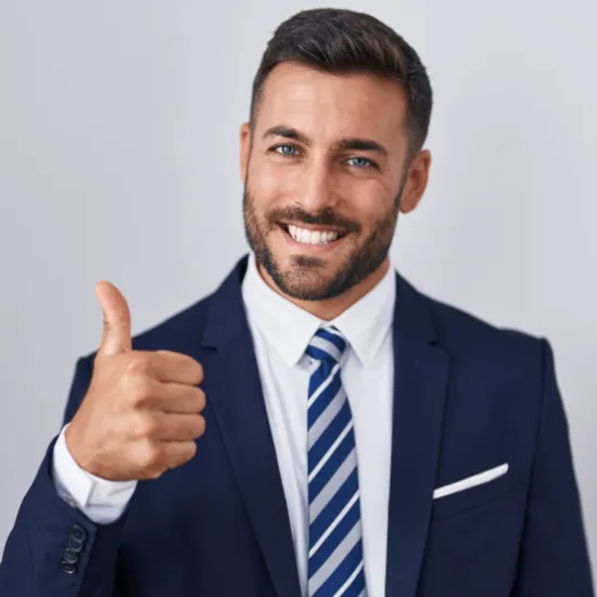 Confident smiling businessman in a navy suit and striped tie giving a thumbs up against a plain light background, symbolizing success, trust, and positive outcomes in professional services.