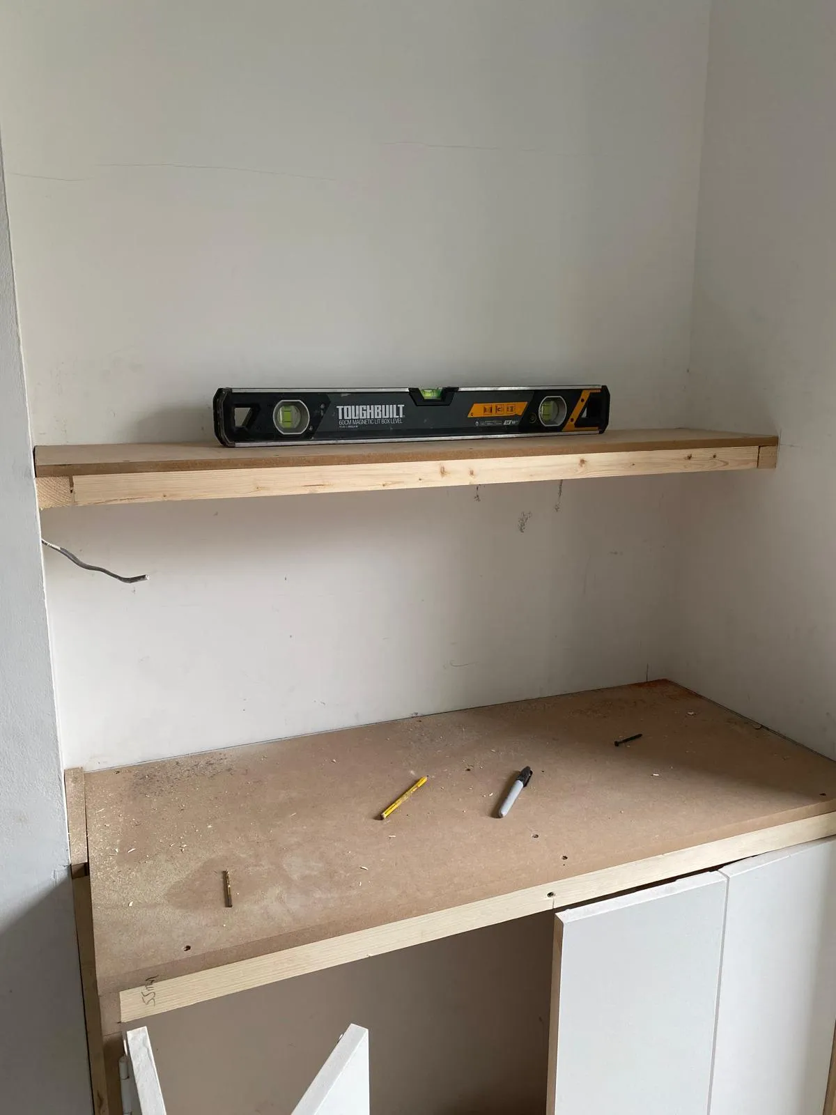 Using a precision green laser level to ensure perfectly vertical alignment for custom cupboard doors in a Surrey alcove storage project.