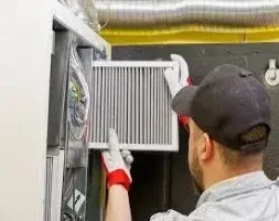 A man is adjusting a furnace in a workshop, surrounded by tools and equipment.
