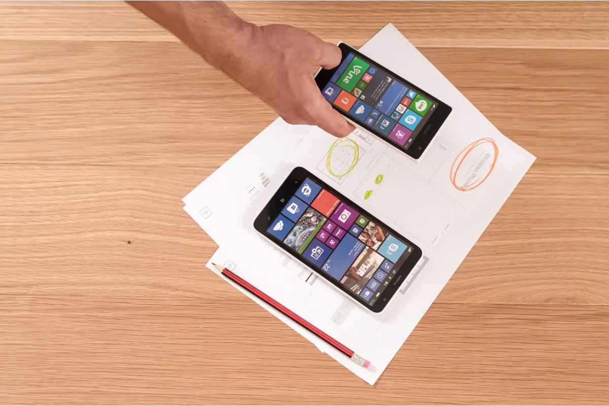 Ariel view of a hand holding a smartphone examining a software interface with paper documents on the table